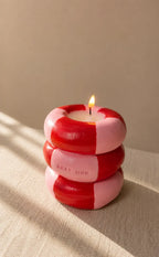 Stacked red and pink candles with a lit candle on a beige surface