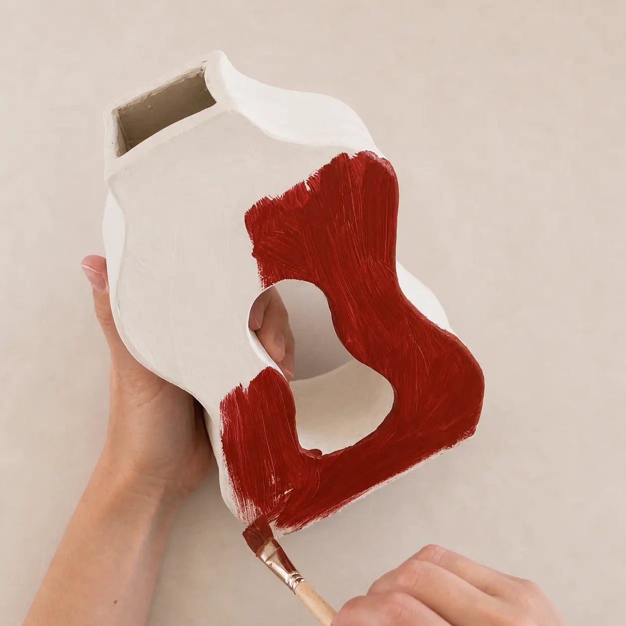 Painting a handmade clay vase with red paint